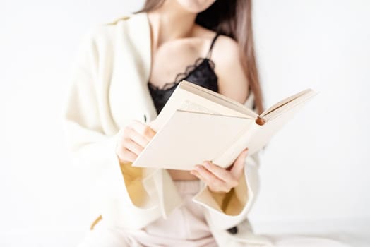 Beautiful smiling woman in comfortable home clothes reading a book sitting on the floor smiling