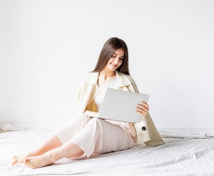 Beautiful smiling young woman sitting on the floor and doing freelance project on laptop, using computer