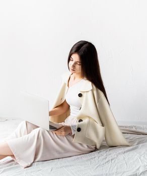 Beautiful young woman sitting on the floor and doing freelance project on laptop, using computer