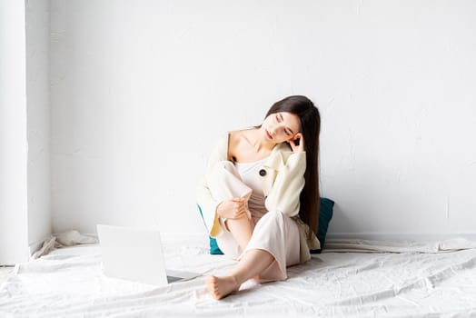 Beautiful young woman sitting on the floor and doing freelance project on laptop, looking away