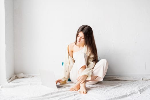 Beautiful young woman sitting on the floor and doing freelance project on laptop, using computer