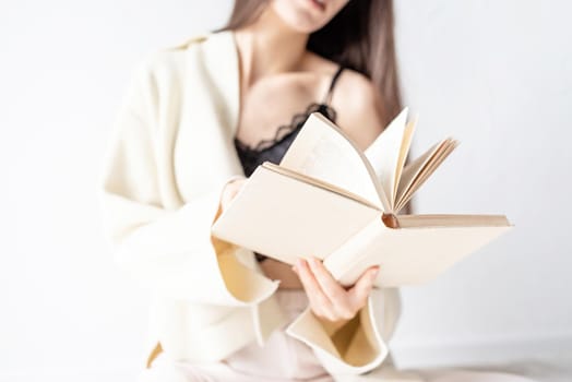 Beautiful smiling woman in comfortable home clothes reading a book sitting on the floor smiling