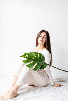 Spa and beauty. Self care and skin care. Happy beautiful woman in cozy clothes holding a green monstera leaf