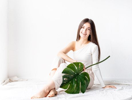 Spa and beauty. Self care and skin care. Happy beautiful woman in cozy clothes holding a green monstera leaf