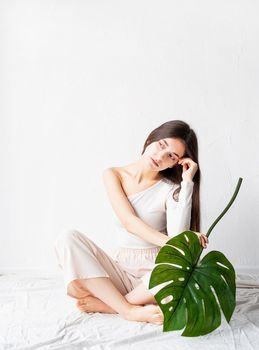 Spa and beauty. Self care and skin care. Happy beautiful woman in cozy clothes holding a green monstera leaf