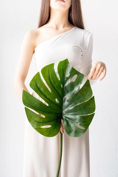 Spa and beauty. Self care and skin care. Happy beautiful woman in cozy clothes holding a green monstera leaf