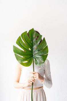 Spa and beauty. Self care and skin care. Happy beautiful woman in cozy clothes holding a green monstera leaf