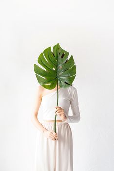 Spa and beauty. Self care and skin care. Happy beautiful woman in cozy clothes holding a green monstera leaf