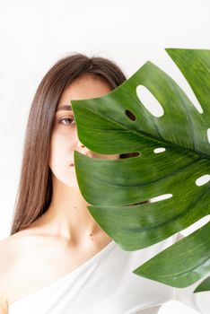 Spa and beauty. Self care and skin care. Happy beautiful woman in cozy clothes holding a green monstera leaf in front of her face