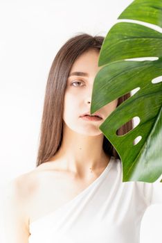 Spa and beauty. Self care and skin care. Happy beautiful woman in cozy clothes holding a green monstera leaf in front of her face