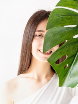 Spa and beauty. Self care and skin care. Happy beautiful woman in cozy clothes holding a green monstera leaf in front of her face