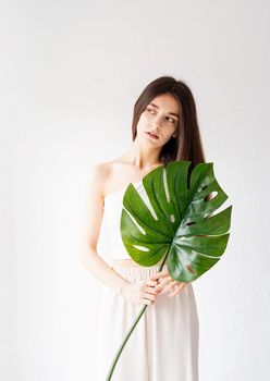 Spa and beauty. Self care and skin care. Happy beautiful woman in cozy clothes holding a green monstera leaf