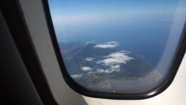 aircraft porthole window with blue sea or ocean in it and small tropical islands. Looking through window aircraft during flight