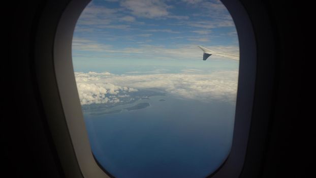 Airplane flying over blue sea and tropical island. Airplane wing through the porthole. Looking through window aircraft during flight
