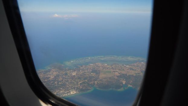 View through an airplane window on the tropical island, ocean, sky and clouds. Aerial view sea, clouds and sky as seen through window of an aircraft. Travel concept.