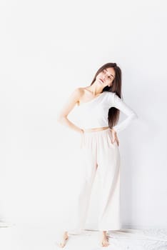 Close up of happy girl in white pajamas standing by the wall at home smiling