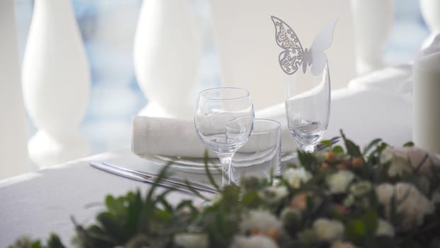 Banquet decorated table, with cutlery. Paper butterfly application on a glass. Wedding decor in the banquet hall. Serving of a festive table, plate, napkin, knife, fork. Table setting decoration. Romantic Dinner or other events.