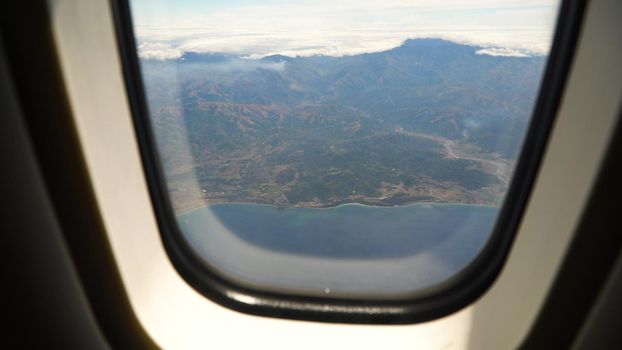 View through an airplane window on the tropical island, ocean, sky and clouds. Aerial view sea, clouds and sky as seen through window of an aircraft. Travel concept.