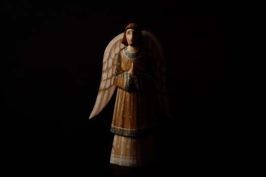 Wooden angel praying with half face in the dark against black background with copy space. High quality photo