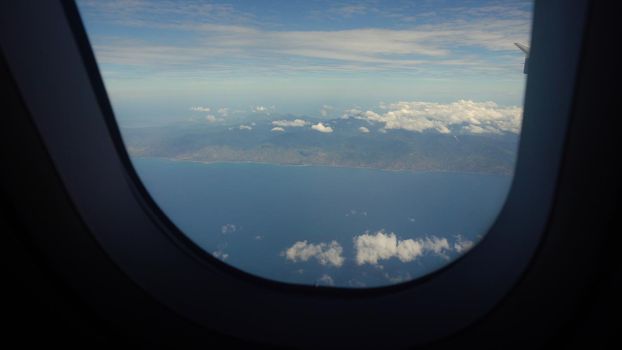 Airplane flying over blue sea and tropical island. Airplane wing through the porthole. Looking through window aircraft during flight