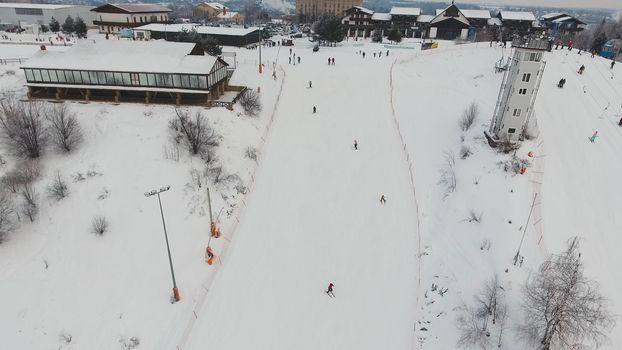 Aerial view: Skiers and snowboarders going down the slope in winter day. Skiers and snowboarders enjoying on slopes of ski resort in winter season.
