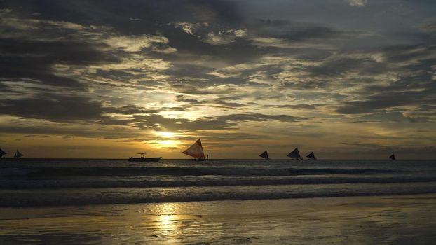 Sunset over the sea in the background boats,sailing boat, orange sky and islands. Sailing boats at sunset in the sea. Travel concept. Beautiful serene scene. Philippines, Boracay. Travel concept.