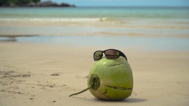 Green coconut on the sand of a tropical beach in sunglasses. Coconut funny wearing sunglasses on the beach. Fresh coconut from palm on a sandy beach. Philippines , El Nido. Travel concept.