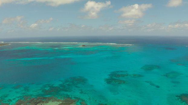Top view of turquoise water of the atoll against the backdrop of the tropical island and sky with clouds. Travel concept.