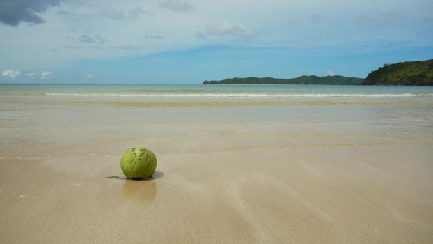 Green coconut on the sand of a tropical beach on a background of blue sky, sea, clouds. Fresh coconut from palm on a sandy beach. Tropical beach, blue sky, clouds.. Philippines El Nido Travel concept.