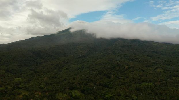 Aerial view of tops of the mountains covered with clouds in the evening Camiguin, Philippines. Mountain landscape on tropical island with mountain peaks covered with forest. Slopes of mountains with evergreen vegetation.