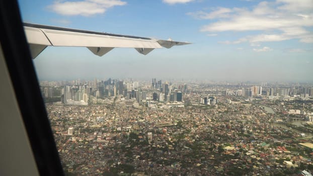 View through an airplane window on the city. Airplane window view showing wing of a plane flying over Manila. Aerial footage, Philippines. Travel concept.