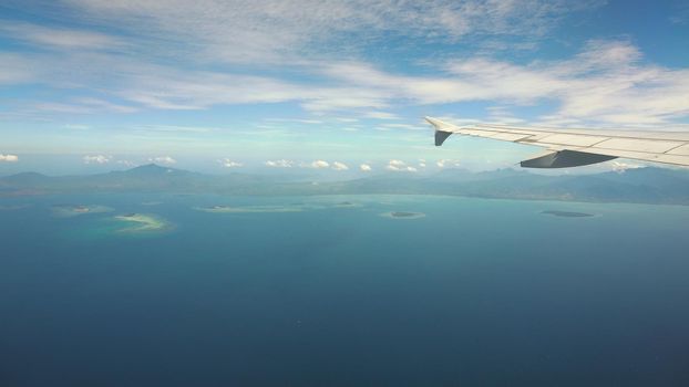 Airplane flying over blue sea and island. Looking through window aircraft during flight