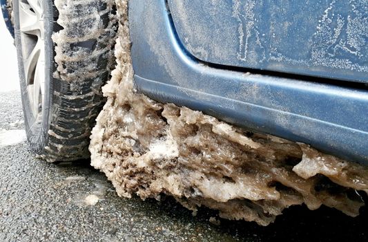 Big frozen snow and ice near wheel and tire under the fender in the wheel arch of the car. Using car on winter road during winter season.