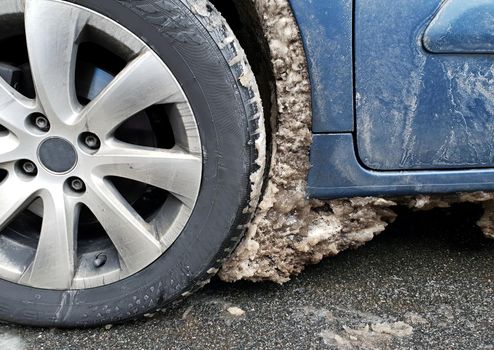 Big frozen snow and ice near wheel and tire under the fender in the wheel arch of the car. Using car on winter road during winter season.