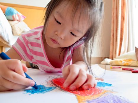 Asian girl Painting crayon on large sheets of paper On the floor of her room