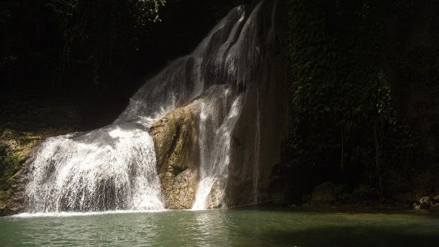 Beautiful waterfall in green forest in jungle. Waterfall with natural swimming pool in a mountain river canyon. Philippines, Bohol.