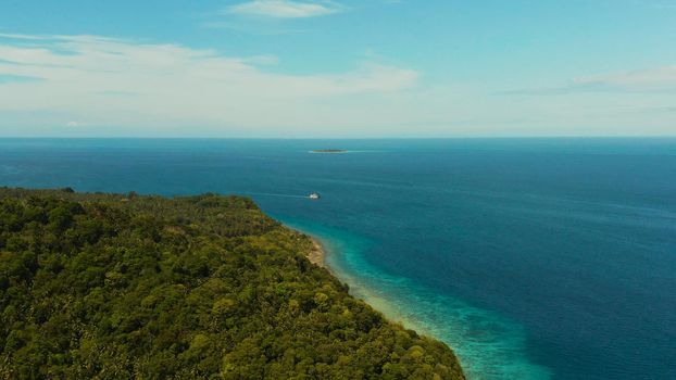 Seascape island coast with forest and palm trees, coral reef with turquoise water, aerial view. Coastline of tropical island covered with green forest against the blue sky with clouds and blue sea