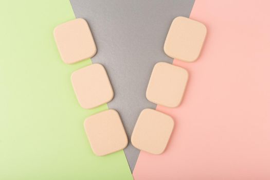 Minimalistic flat lay with with two rows of square shaped make up sponges against colored pink, silver and green background. High quality photo