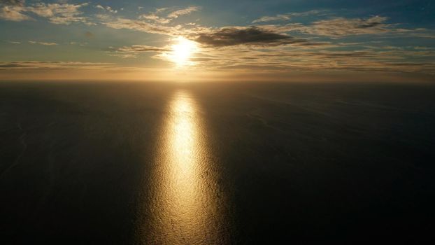 Sunset above the sea surface with waves, aerial drone. Reflected sun on a water surface. Sunset over ocean. Seascape, Summer and travel vacation concept