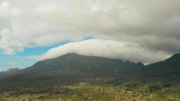 Aerial view of mountains covered rainforest, trees. Camiguin, Philippines. Mountain landscape on tropical island with mountain peaks covered with forest. Slopes of mountains with evergreen vegetation.