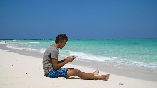 Man using electronic tablet on the beach. Man sits on a sandy beach and using a tablet. Tropical beach, blue sky, clouds. Philippines, Travel concept.