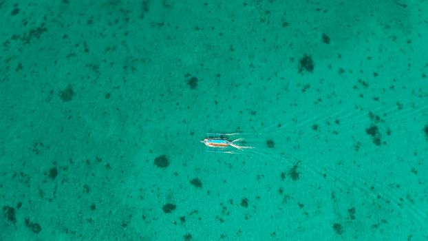 Tourist motor boat on the surface of turquoise water in tropical lagoon, aerial view. Seascape with beach on tropical island. Summer and travel vacation concept. Boracay Island, Philippines