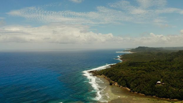 The coast of Siargao island with beach, green forest and ocean surf with waves against the sky and clouds, aerial view. tropical landscape.