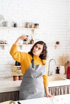 Beautiful brunette woman in yellow sweater and gray apron coloring easter eggs in the kitchen holding test tube with orange color