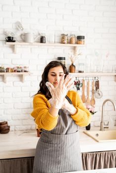 Beautiful brunette woman in yellow sweater and gray apron preparing to color easter eggs in the kitchen putting on the gloves