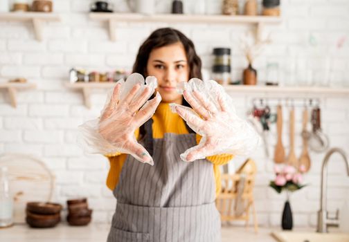 Beautiful brunette woman in yellow sweater and gray apron preparing to color easter eggs in the kitchen putting on the gloves