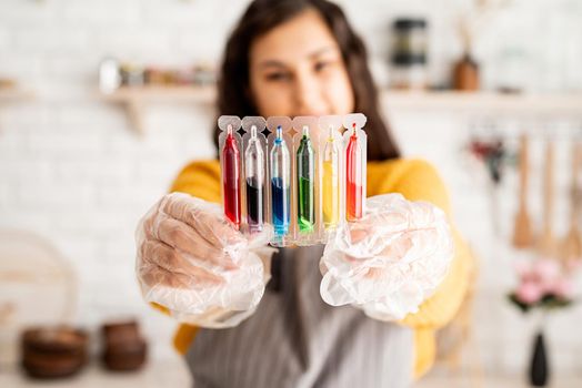 Beautiful woman coloring easter eggs in the kitchen holding tubes with colorful liquids