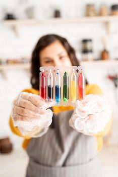 Beautiful woman coloring easter eggs in the kitchen holding tubes with colorful liquids