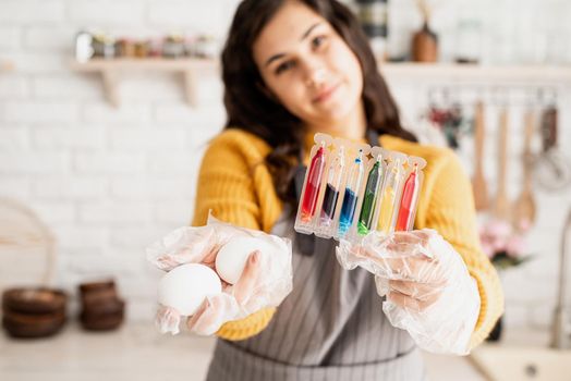 Beautiful woman coloring easter eggs in the kitchen holding tubes with colorful liquids and white eggs
