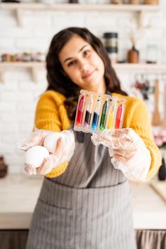 Beautiful woman coloring easter eggs in the kitchen holding tubes with colorful liquids and white eggs